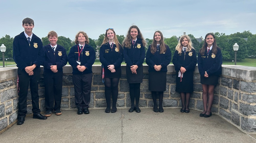 group of students standing outside in front of gray landscape wall wearing blue FFA jackets