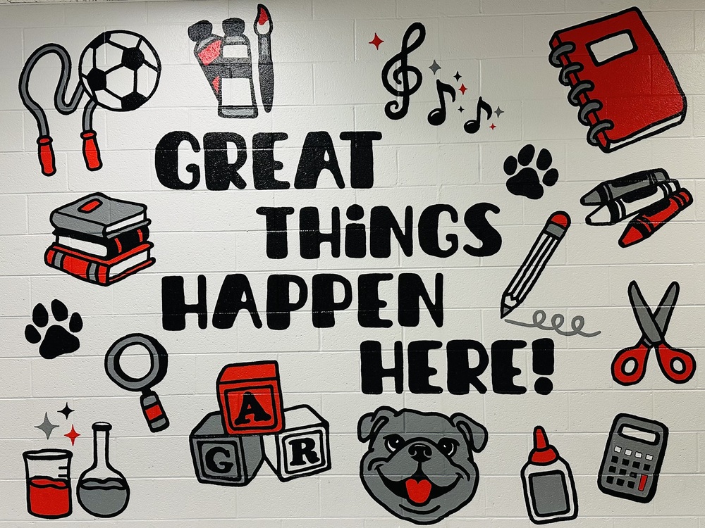 A colorful mural at A.G. Richardson Elementary School reads “Great Things Happen Here!” surrounded by red, black and gray illustrations representing learning and school activities, including books, art supplies, musical notes, sports equipment, science beakers, a pencil, scissors, a calculator, paw prints and a bulldog mascot.