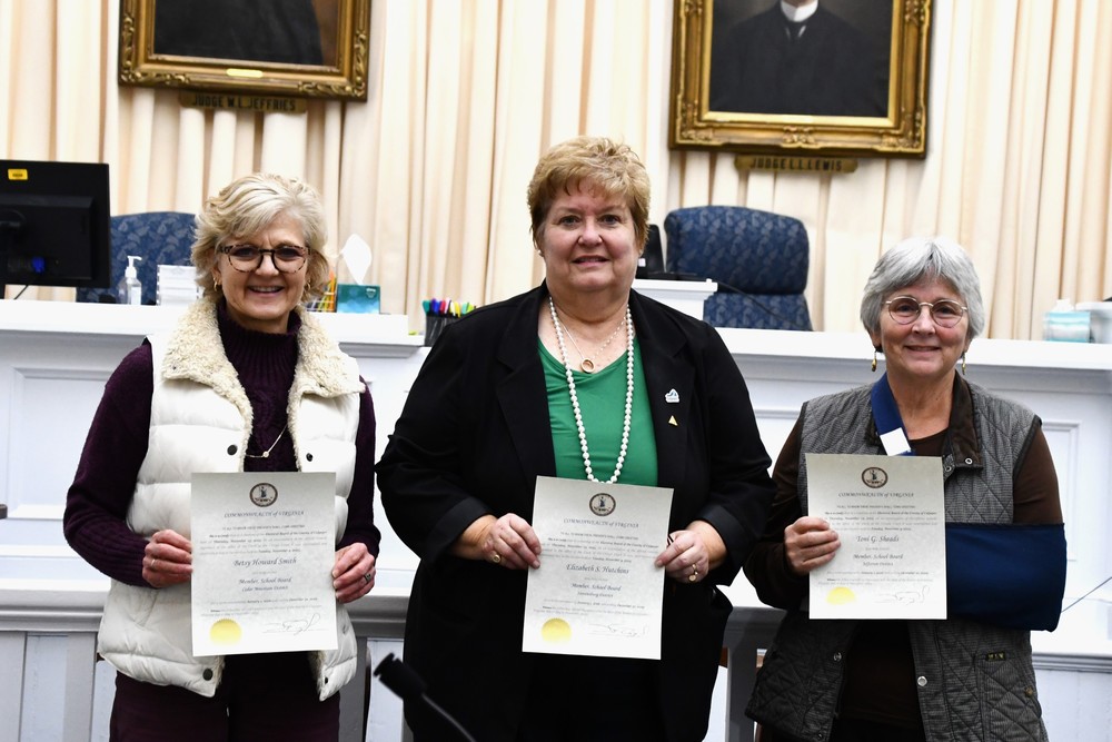three board members standing in a courtoom holding up certificates with portraits of judges behind them