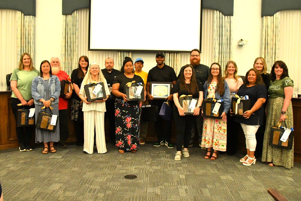 group of school employees standing in board room holding gift bags and certificates