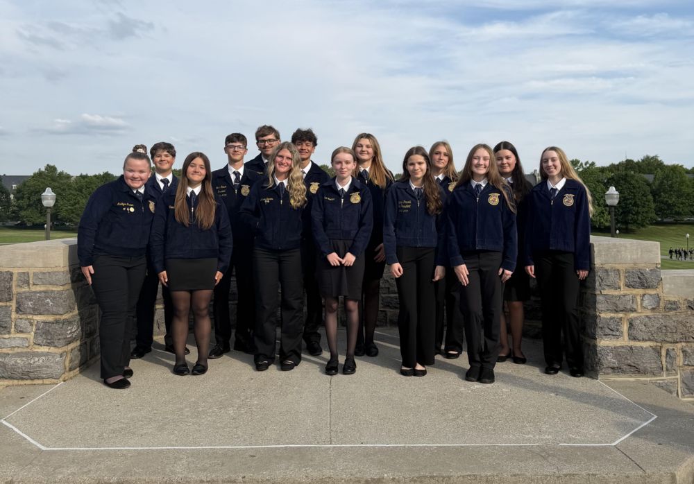 group of students standing outside in front of gray landscape wall wearing blue FFA jackets