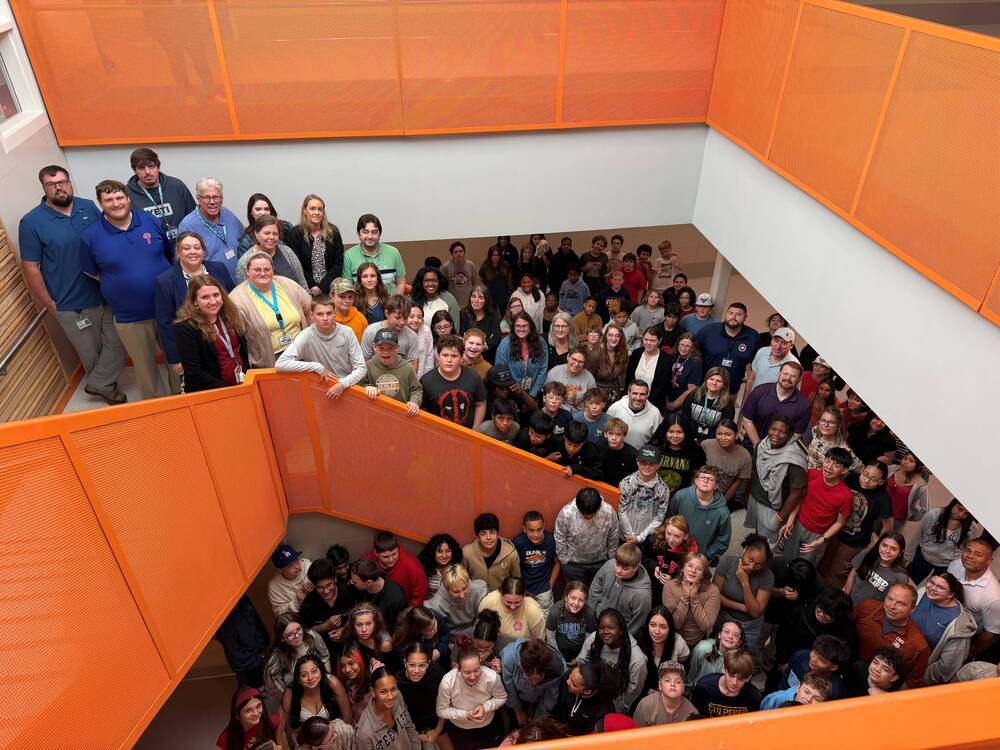 students and staff in a large stairwell with orange railings 