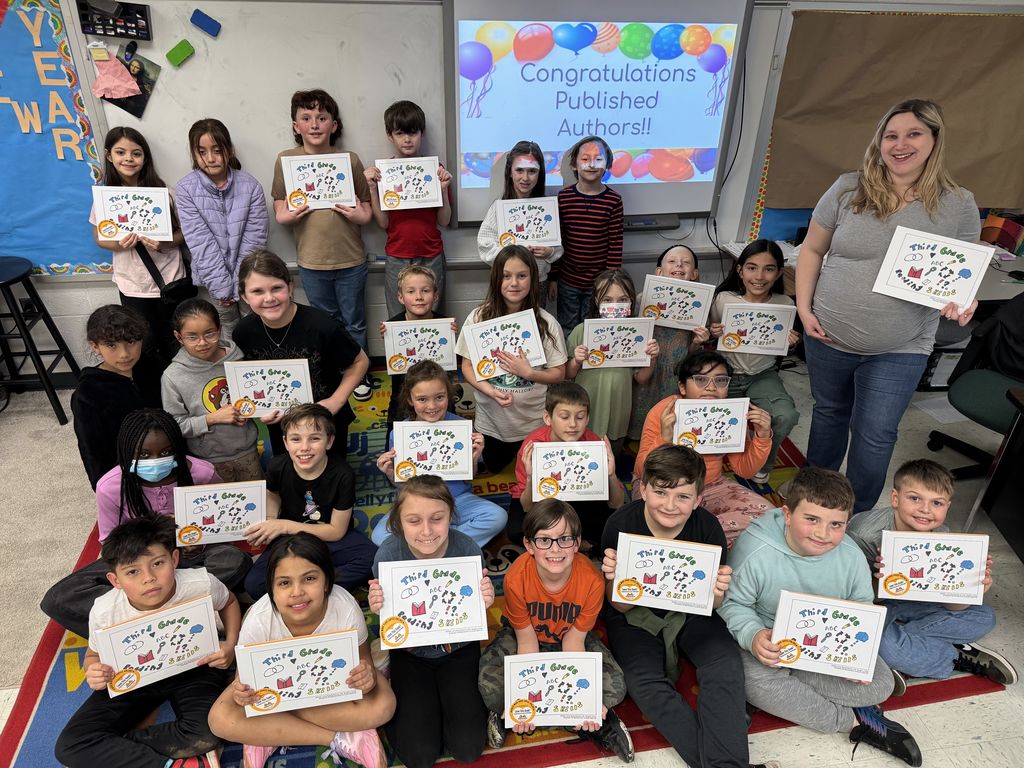 A group of students and their teacher holding up copies of their self published book with a sign behind them reading "Congratulations published authors!"