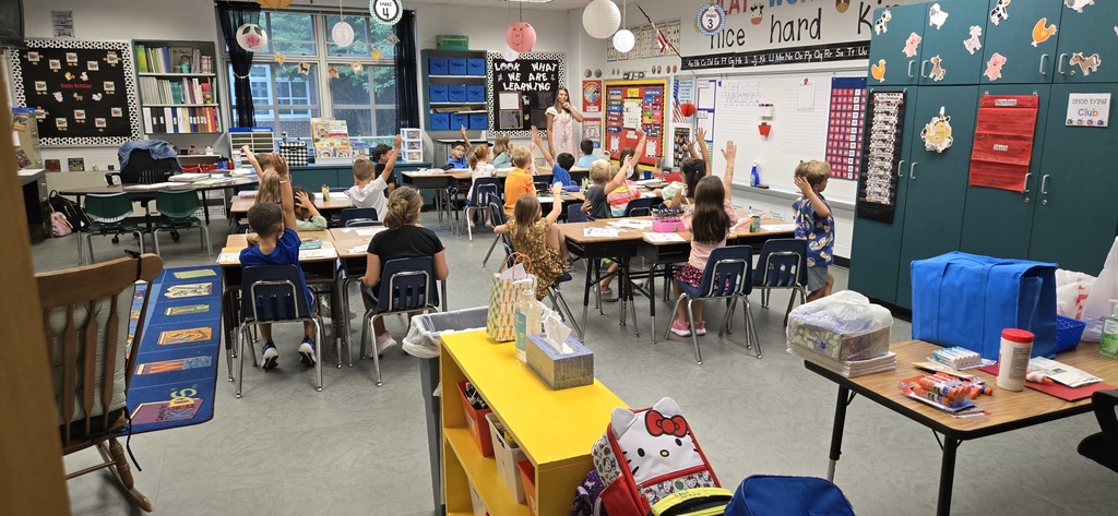 First grade teacher asking a question with a group of students raising their hands