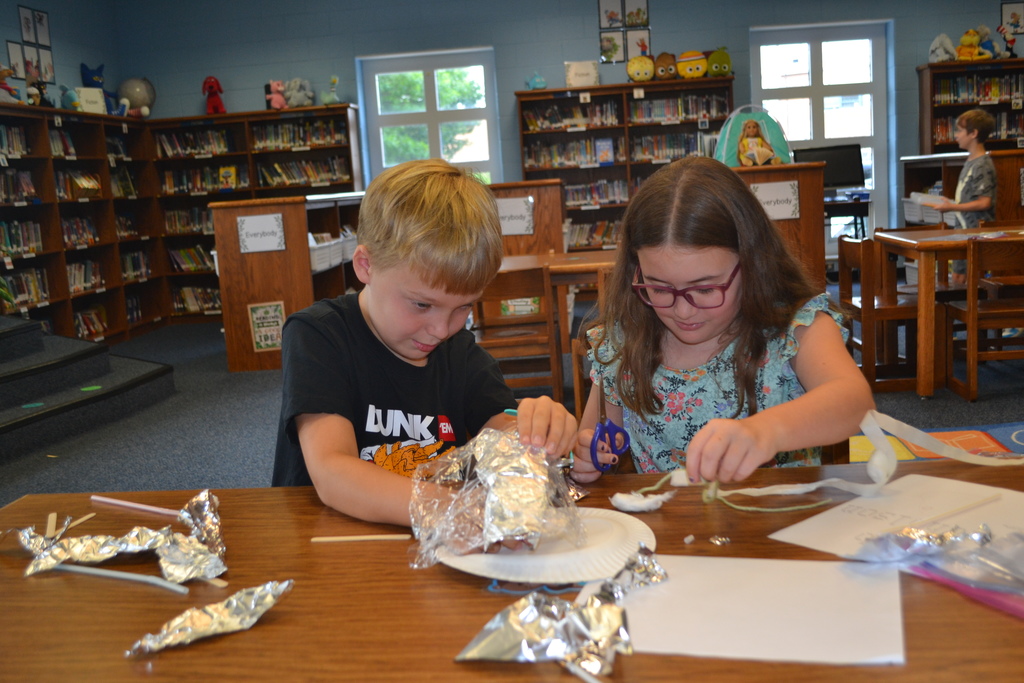 Image contains two students work together, with concentrated looks,  using the materials provided to build a "tent".