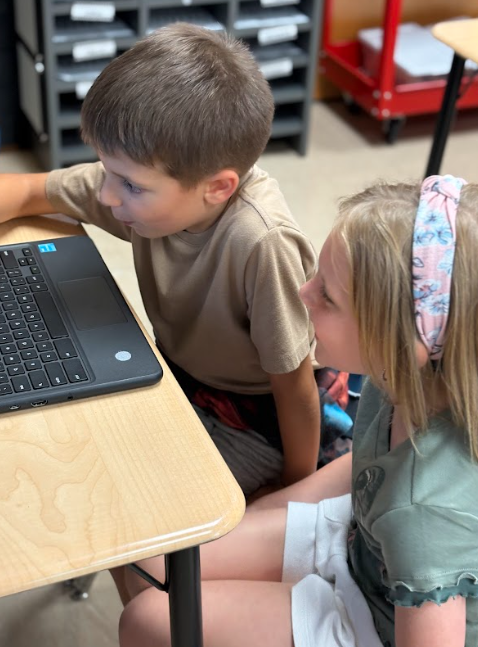 A boy and girl sitting side by side, focused on a laptop screen together.