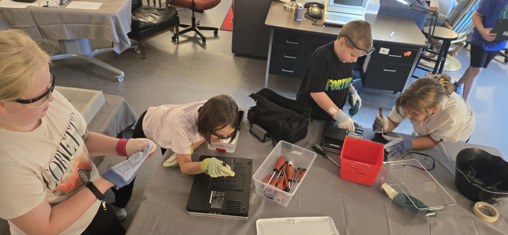 Students wearing safety goggle and gloves disassembling old laptops.