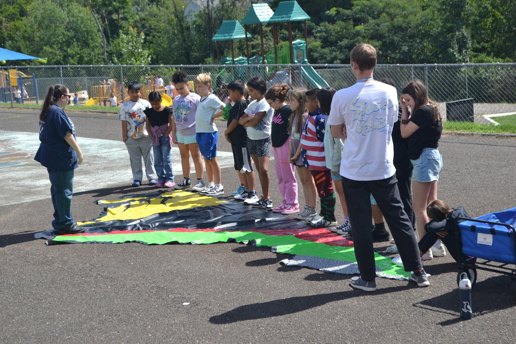 Image contains a group of students outside with the guest presenter.  There is a large duck tape map of Virginia.  Teacher is on the far right of the image.