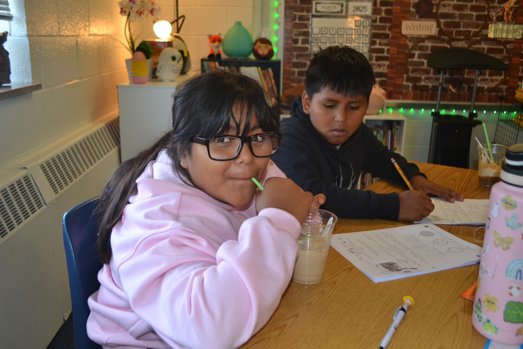 Student A drinks her root beer float while student B fills out his paper at their desk.