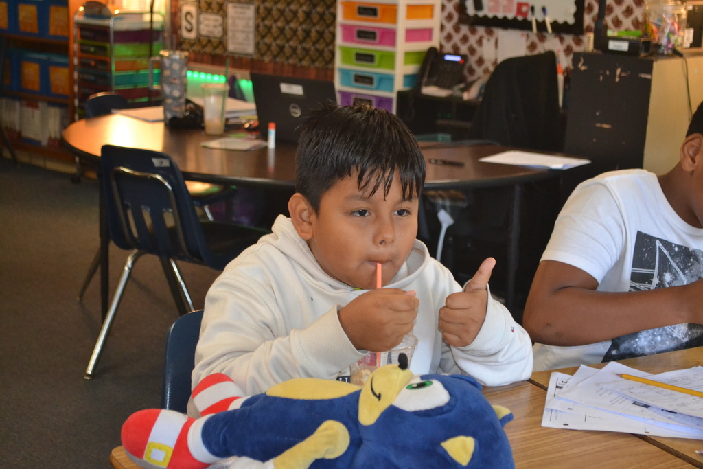 Student gives a thumbs up while sipping his root beer float at his desk.