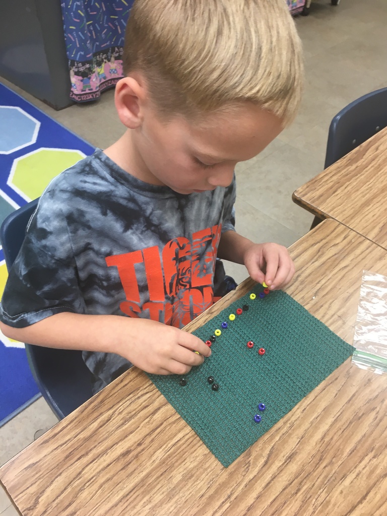 student in black tie dye shirt using colorful beads to make a pattern