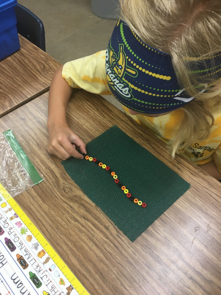 student in a blue, yellow, and green headband creating a pattern with beads