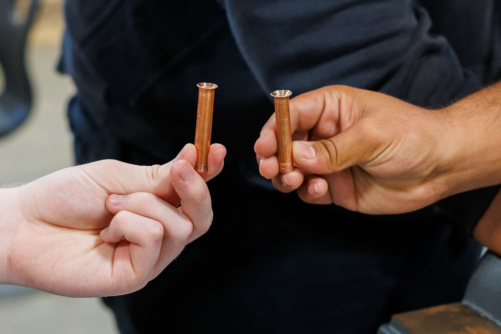 Close-up of two students’ hands holding flared copper tubing pieces side by side, comparing their work.