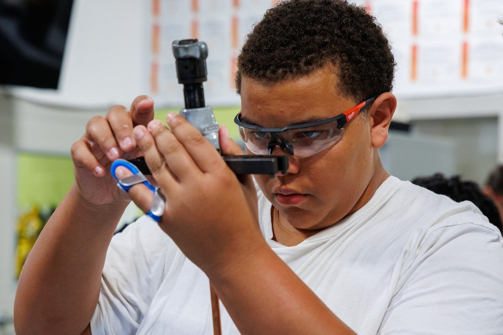 A student in safety glasses concentrates while using a flaring tool on copper tubing during hands-on HVAC practice.