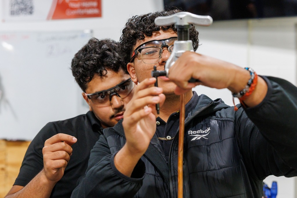 Two students carefully adjust a flaring tool on copper tubing, focusing closely as they practice the HVAC skill.