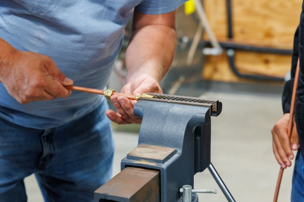 An instructor demonstrates how to secure a copper tube in a vise, showing students the proper setup for flaring.