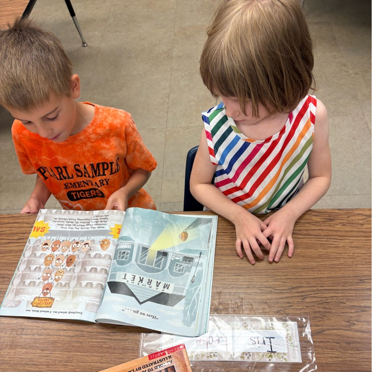 a boy in an orange shirt and a girl in a rainbow striped shirt read a book together
