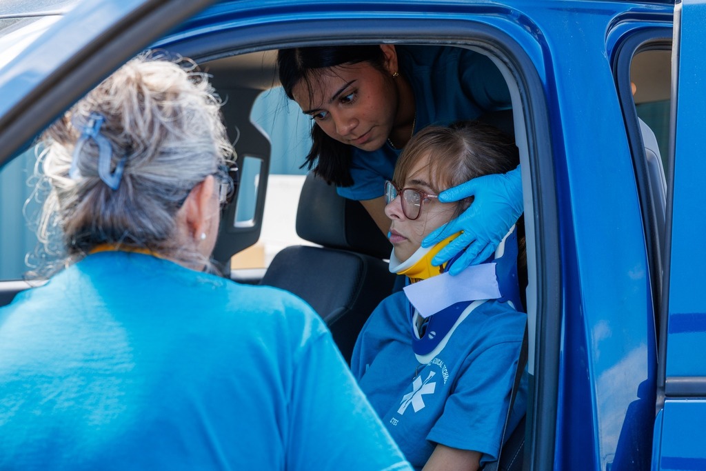 A student carefully stabilizes a classmate wearing a neck brace inside the truck, while an instructor observes and provides guidance.