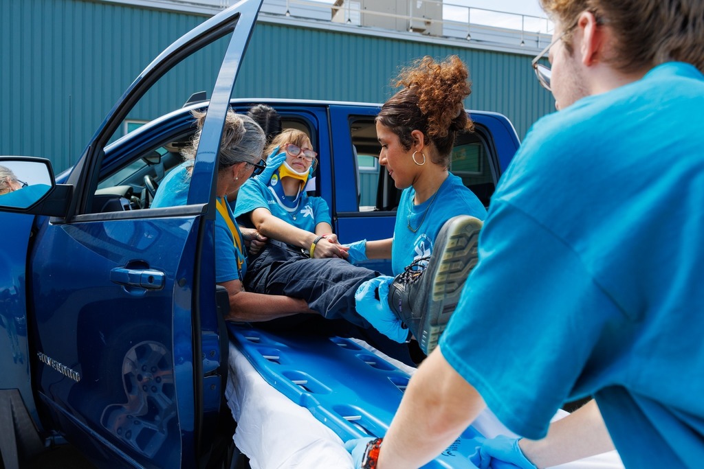 EMT students and their instructor work together to carefully lift the patient from the truck onto a backboard, ensuring spinal precautions.