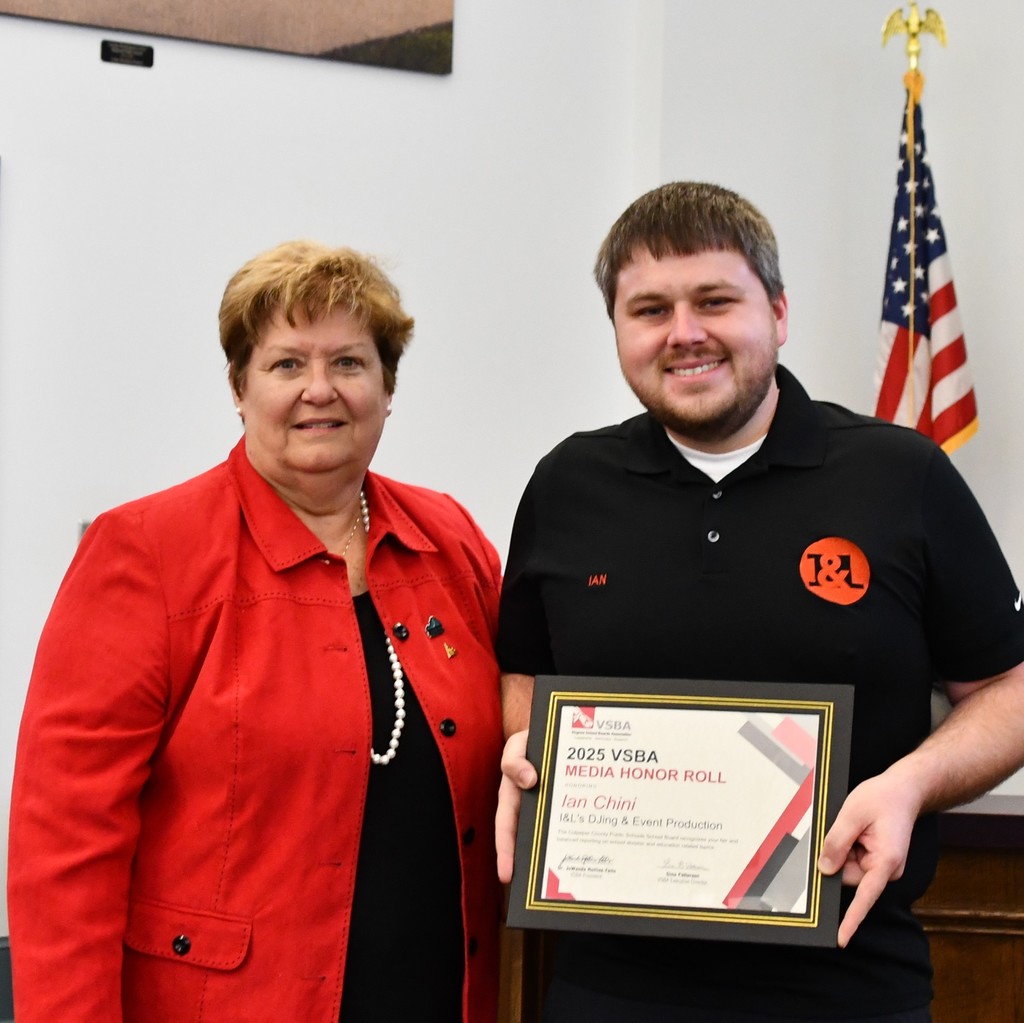 A Culpeper County School Board member presents a framed 2025 VSBA Media Honor Roll certificate to a representative from I&L DJ and Events. Both are smiling and standing together in front of an American flag.