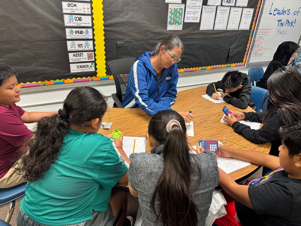 A close-up of Mrs. Carter leading a group discussion at a round table. Students are engaged with calculators and pencils while looking at worksheets.