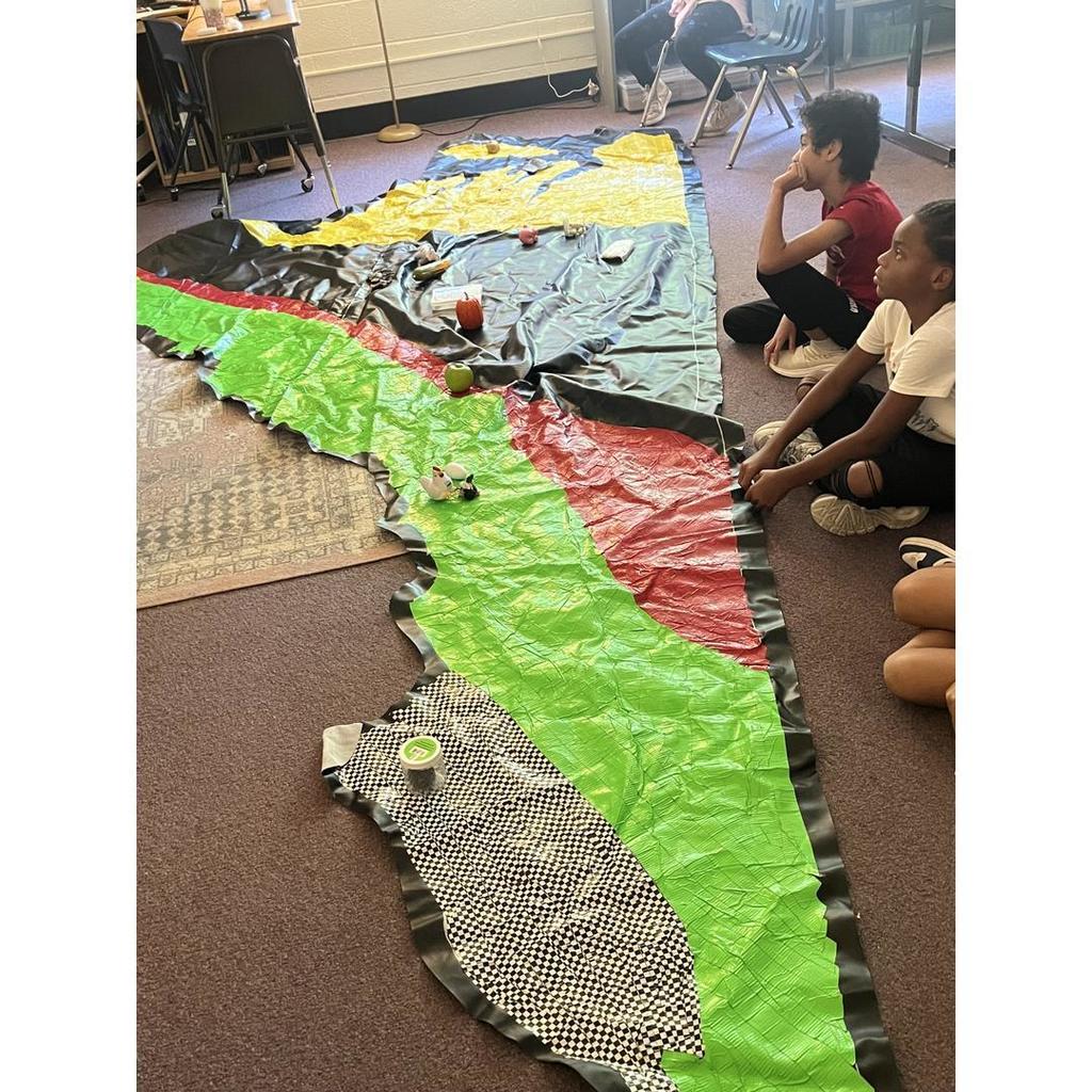 Two students sit near the map of Virginia’s regions, studying the objects placed on it.
