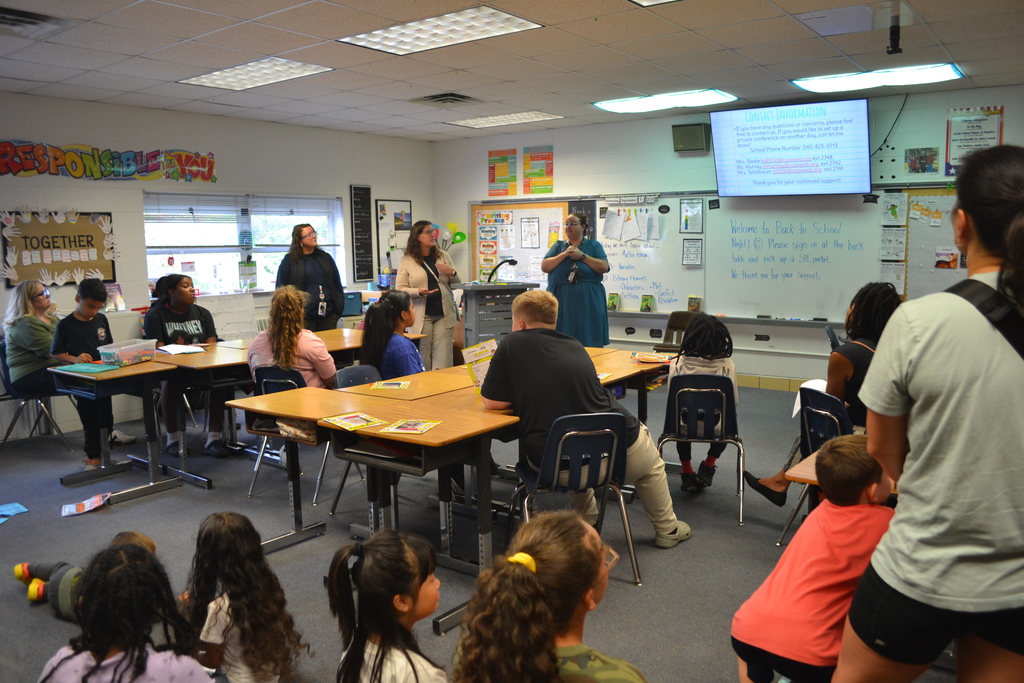 Image contains a classroom where 3 teachers are presenting information to families at Back to School Night.