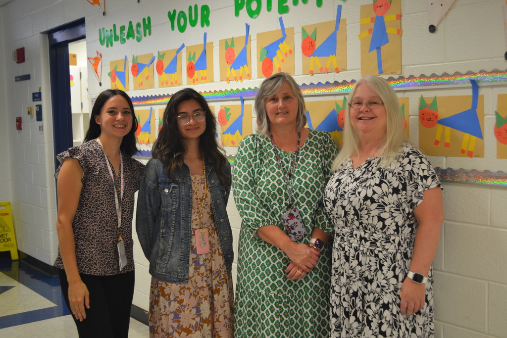 Image contains 4 teachers smiling and posing for the camera in the school hallway.