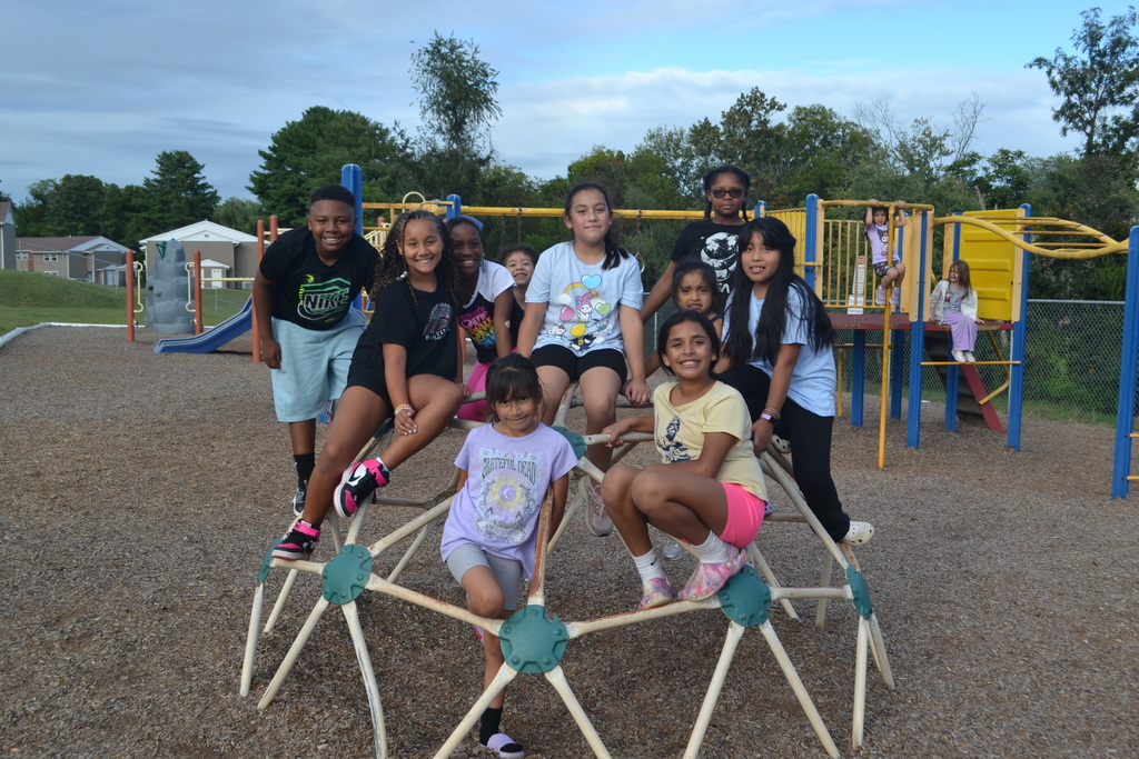 Image contains a group of 10 students climbing on a playground equipment on the playground.