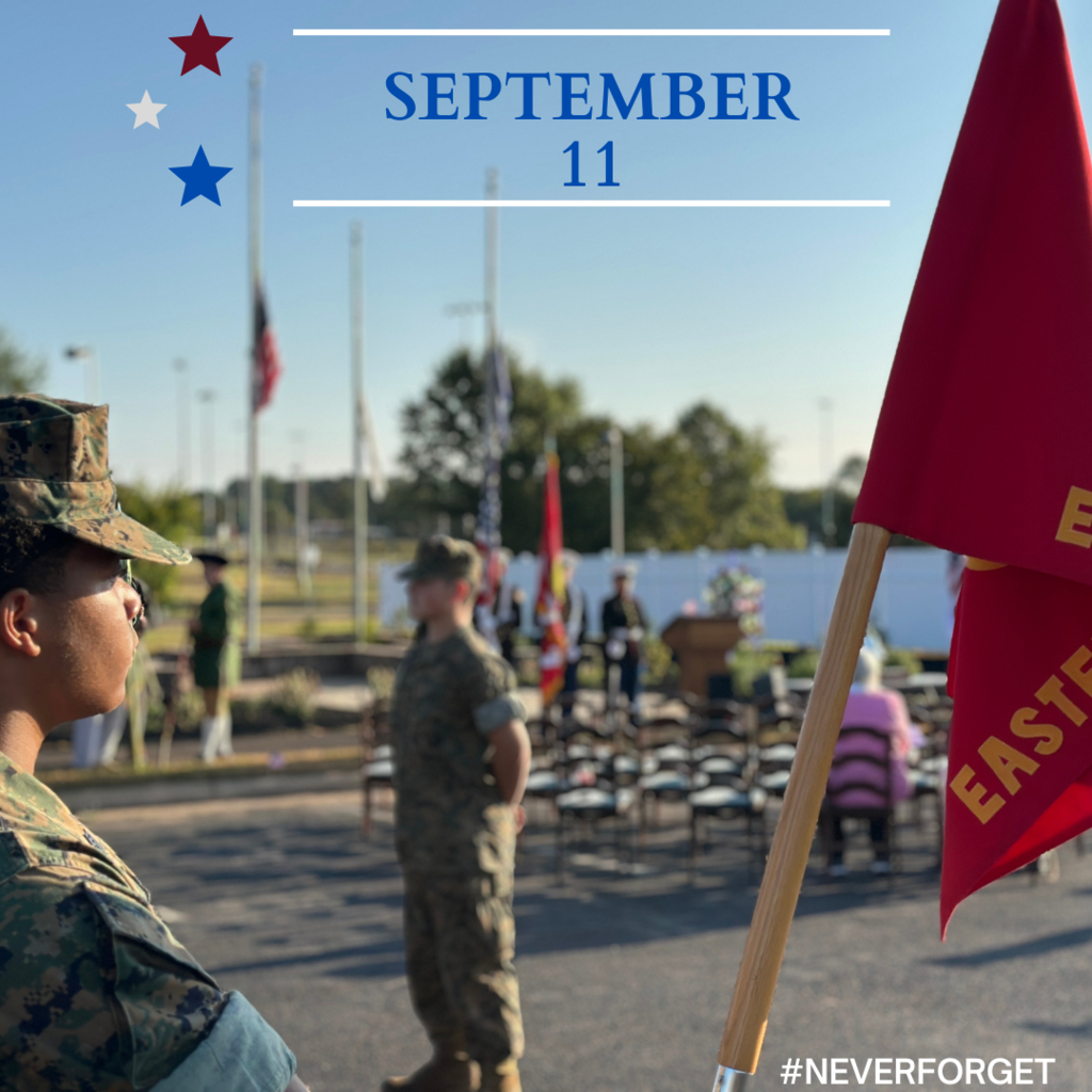 U.S. Marine Corps JROTC cadets stand in formation during a September 11 remembrance ceremony. A red unit flag reading ‘Eastern View’ is in the foreground, with American flags flying at half-staff in the background. The text ‘September 11’ appears at the top with red, white, and blue stars, and the hashtag #NeverForget is displayed in the corner.”
