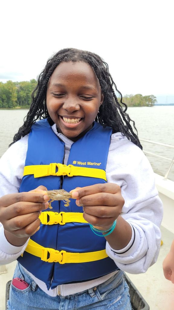 student in life vest smiles broadly while holding crab trawled from theJames River.