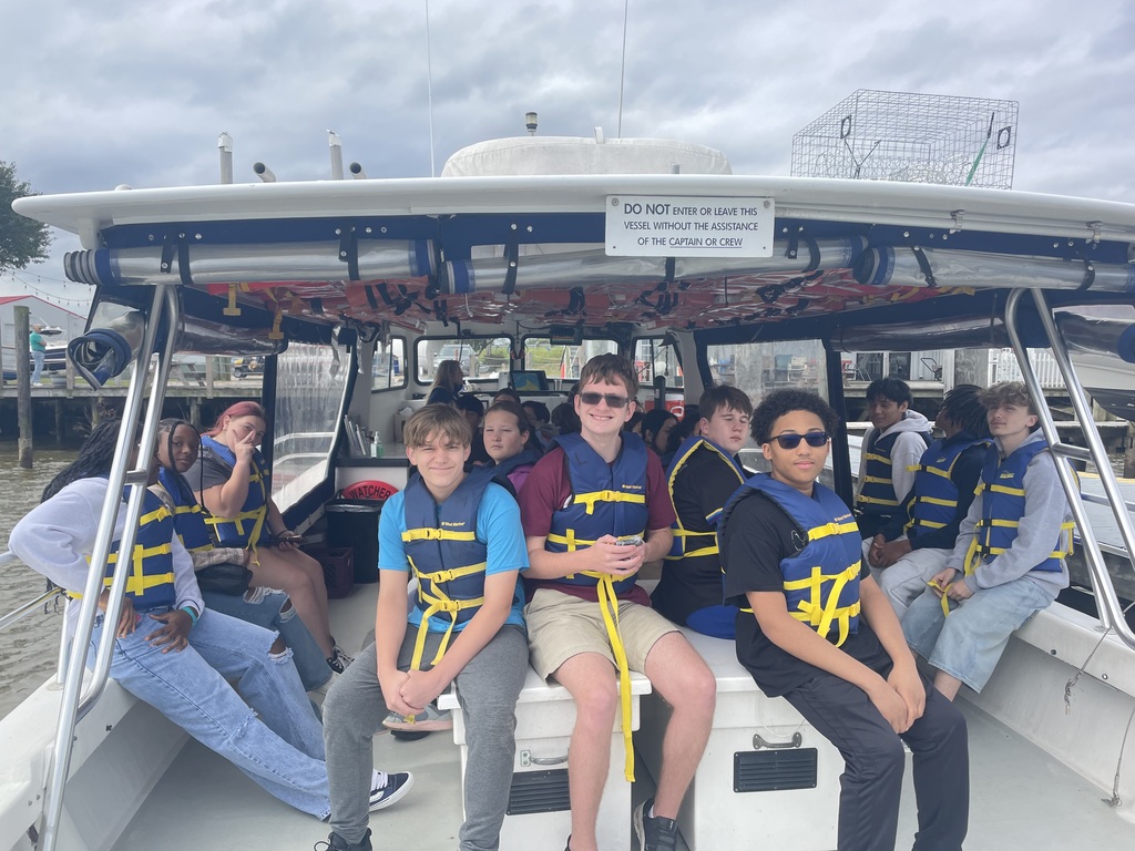 Students in life vests smile for the camera while sitting on a boat .