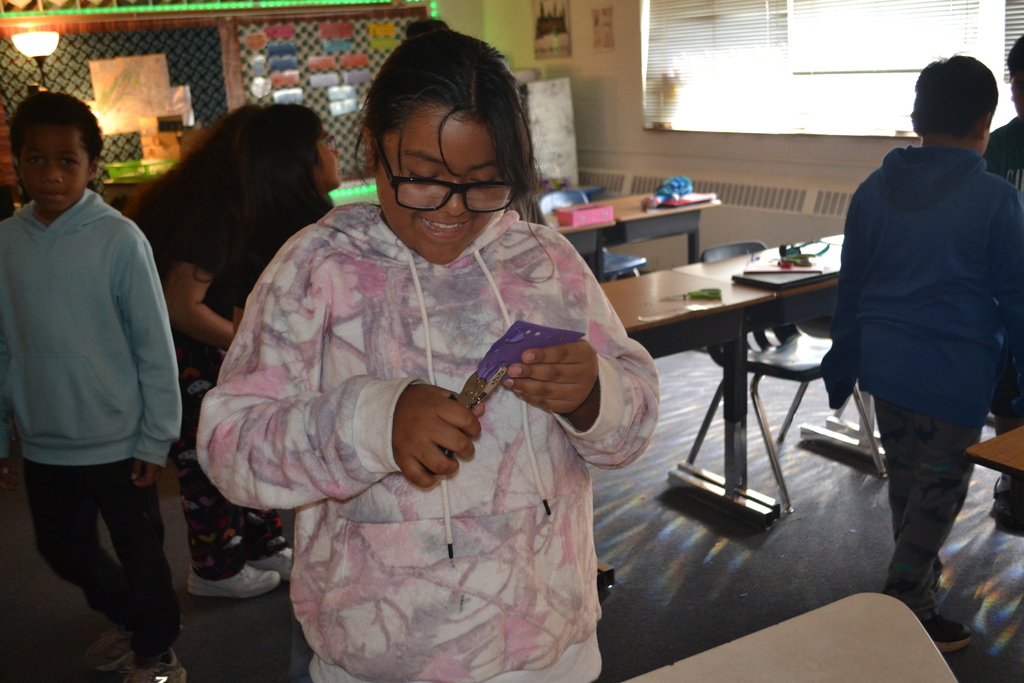 Image contains a student creating her papel picado artwork.  Other students are working in the background.