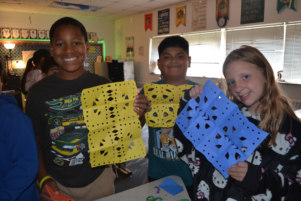 Image contains 3 students proudly showing their papel picado artwork in their classroom.