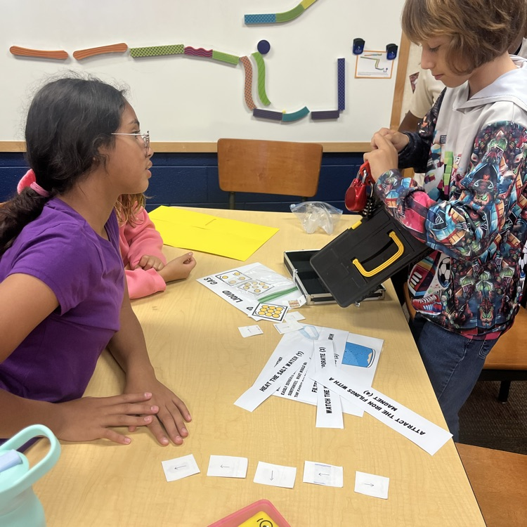 two students work together to open a lock on a lock box after solving a science clue about matter 