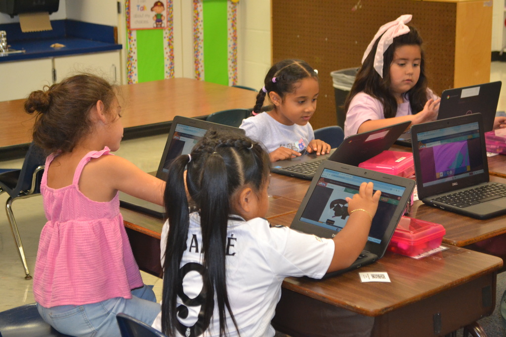 Image contains a 4 kindergartners each on their chromebook in a classroom.  Each student is learning to use their chromebook.
