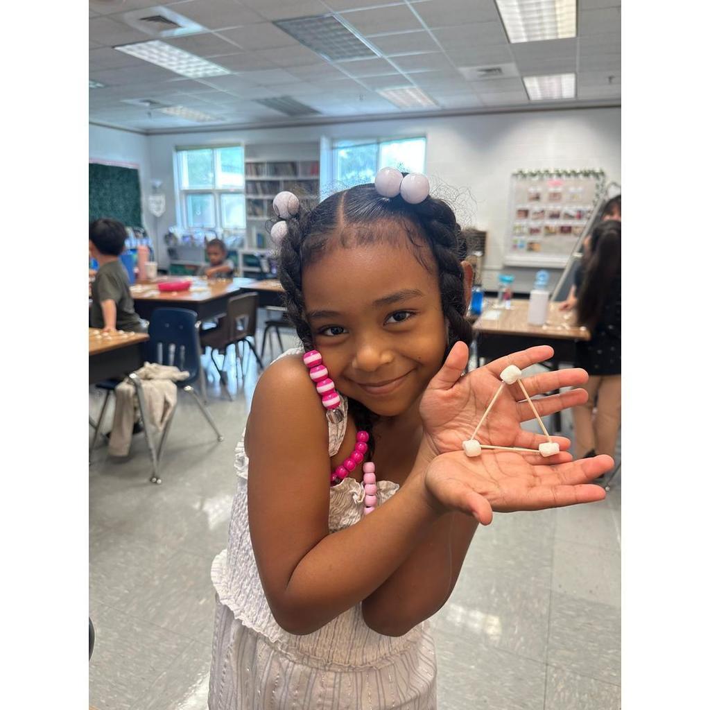 A student proudly holds up a small triangular marshmallow and toothpick structure in their hands.