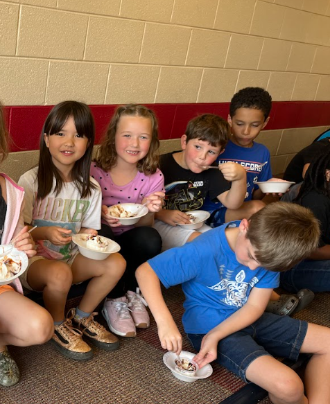 A group of students sit in a row, holding bowls of ice cream and smiling at the camera.