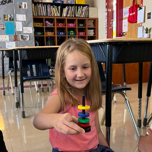 A girl in a pink shirt smiles while holding a stack of colorful magnetic rings she has put together.