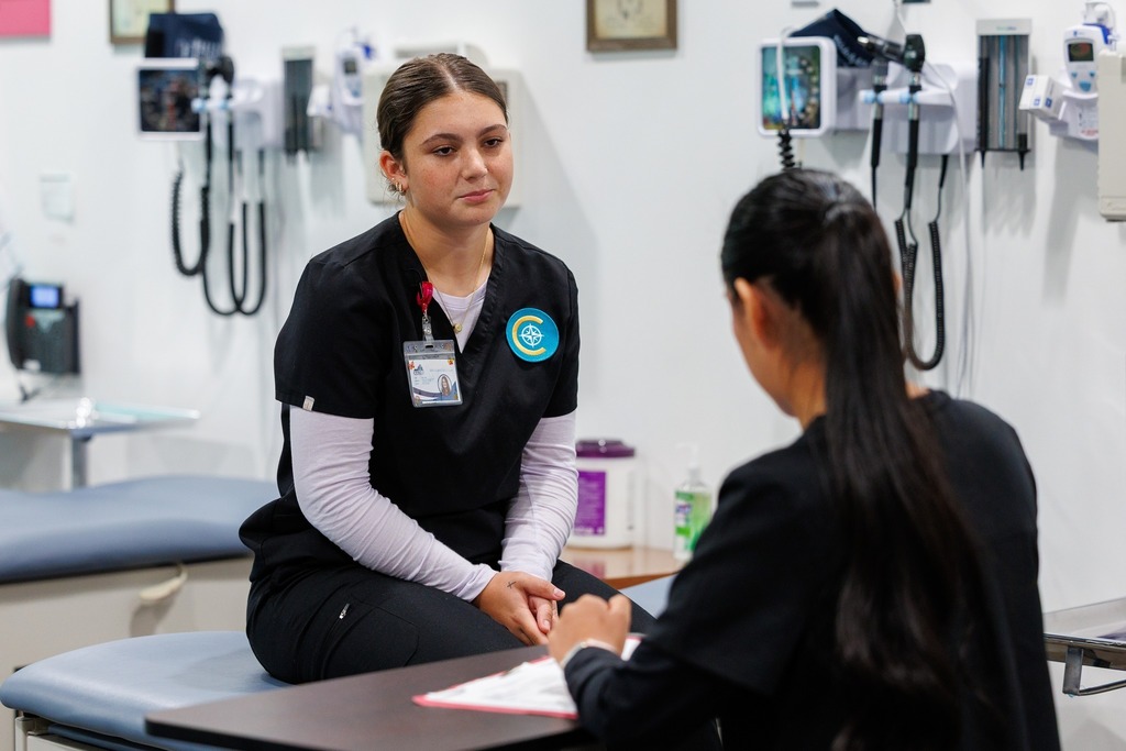A CTEC medical assistant student on an exam table listens carefully to her classmate conducting the patient interview.