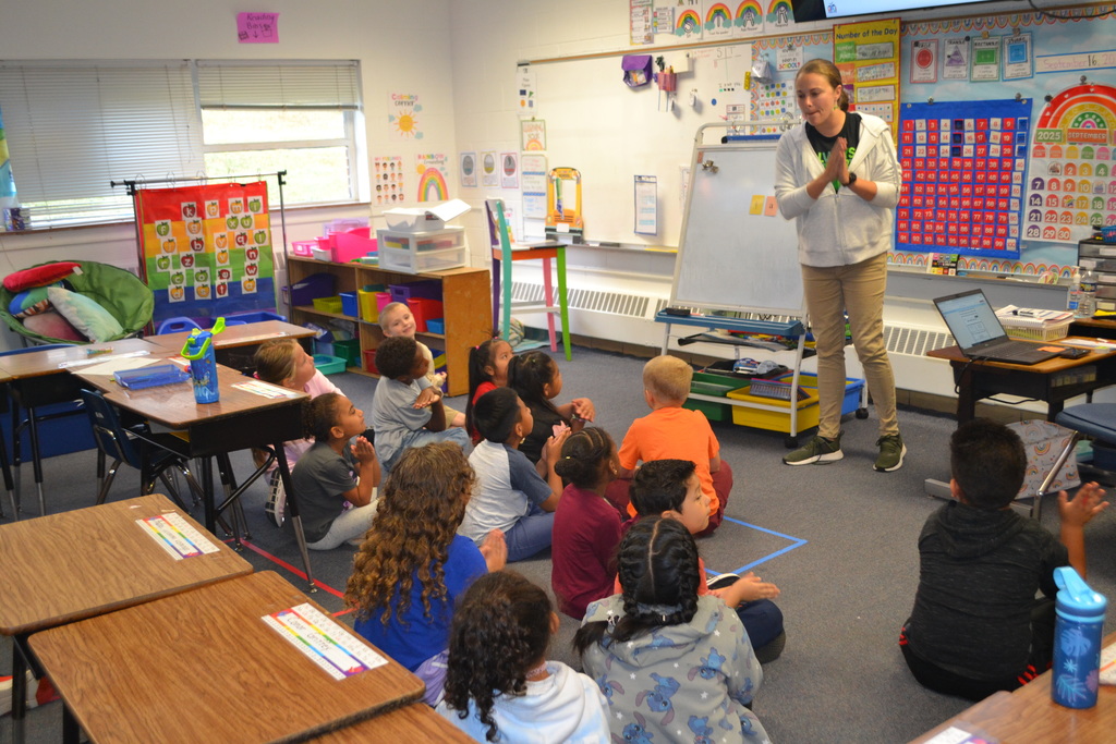Image contains a teacher clapping syllables while her class sits in front of her practicing the same skill.