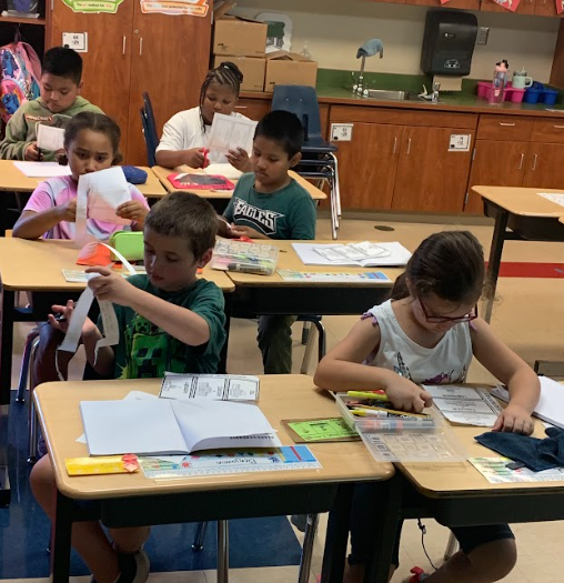 Several students sit at desks cutting and coloring worksheets. They appear focused as they work on interactive notebook activities.
