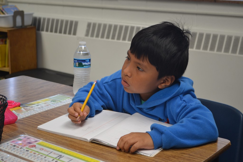 A student looking at the teacher from his desk in the school classroom.