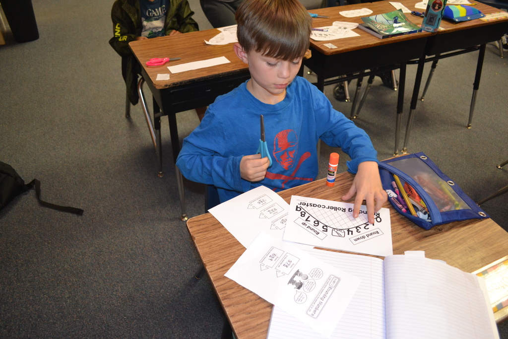 A boy is doing his math sheet at his desk in a classroom.