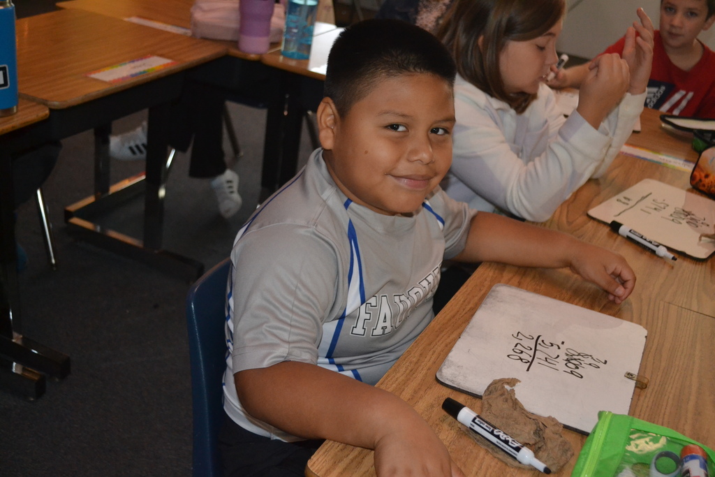 A student is smiling at a the camera with math on his white board.