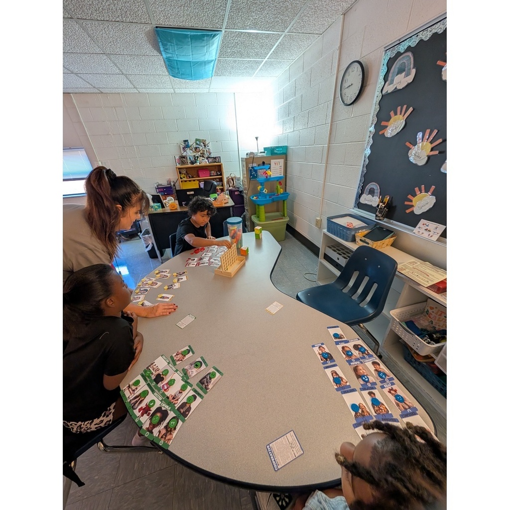 Small group classroom activity — A teacher works with students seated at a table playing a character-based card game and connect-four.