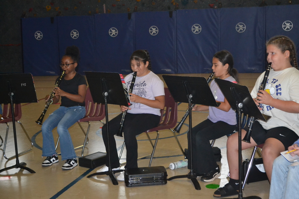 Four students in chairs with music stands playing their instruments at practice in the school gym.