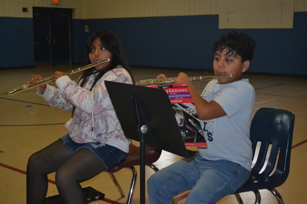Two students in chairs with music stands playing their instruments at practice in the school gym.