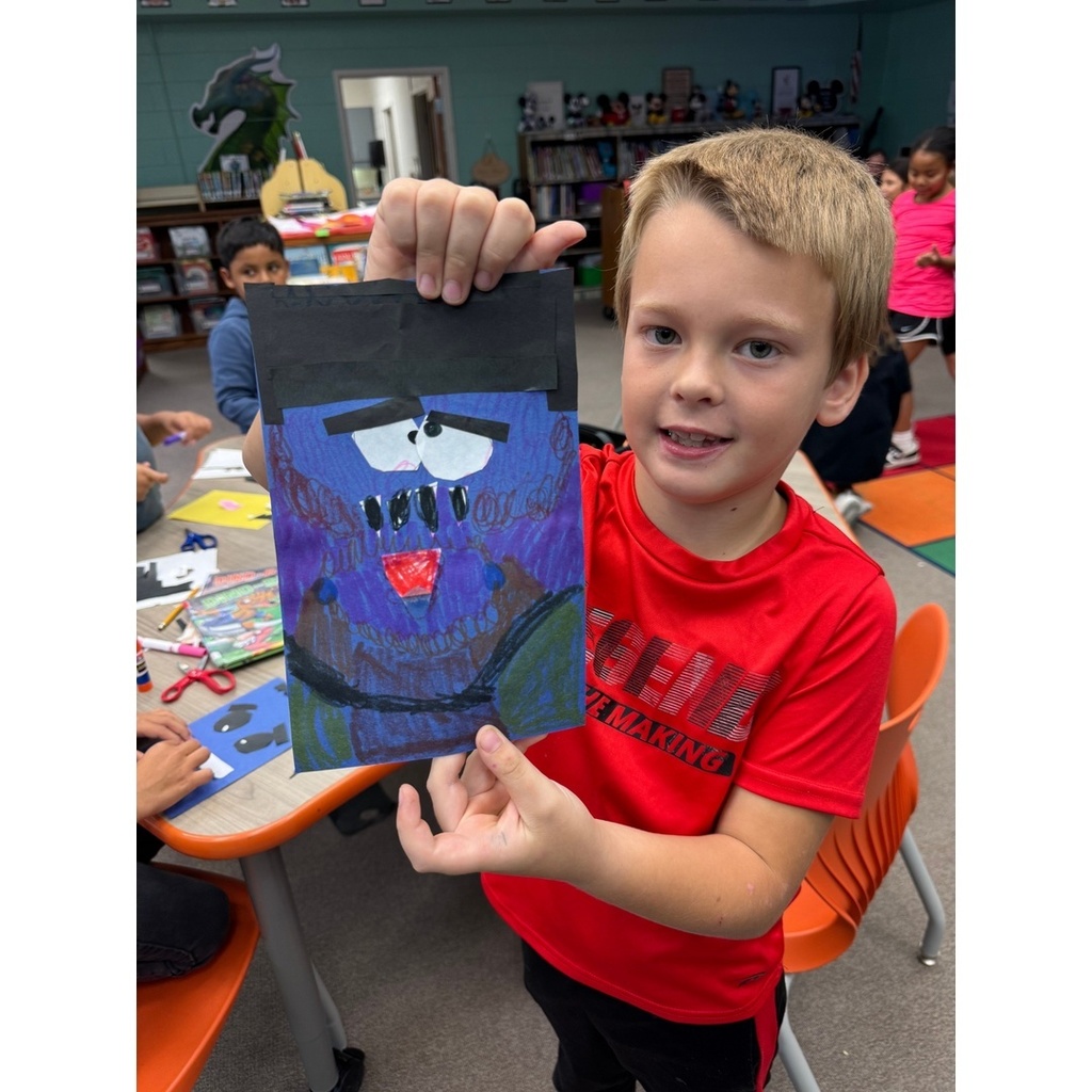 A child in a red shirt shows off a detailed purple and black monster face craft.