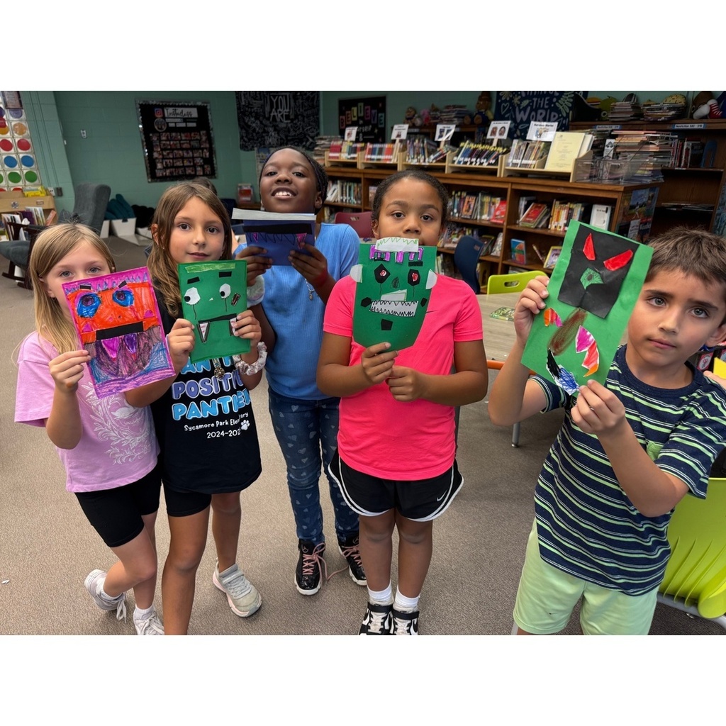 Five students stand together holding up colorful paper monsters they made.